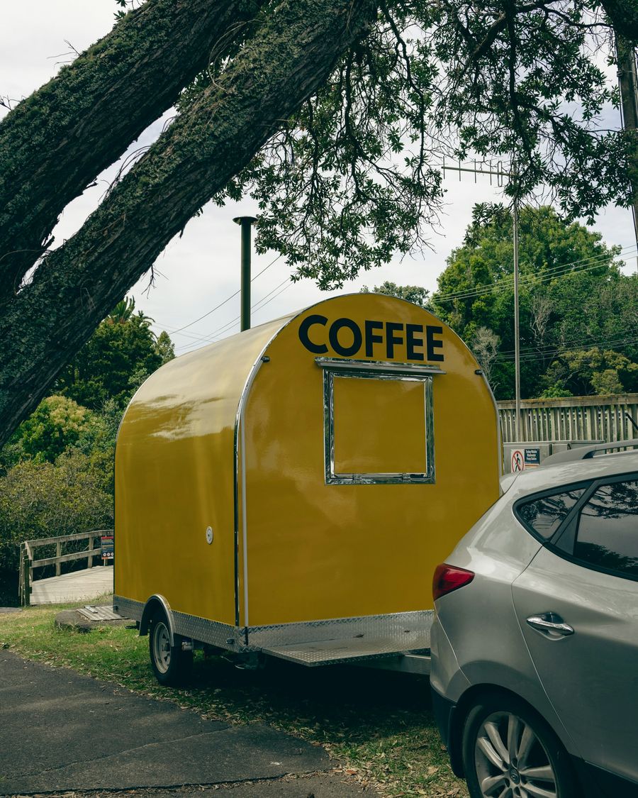 A yellow mobile coffee trailer parked near an Auckland beach