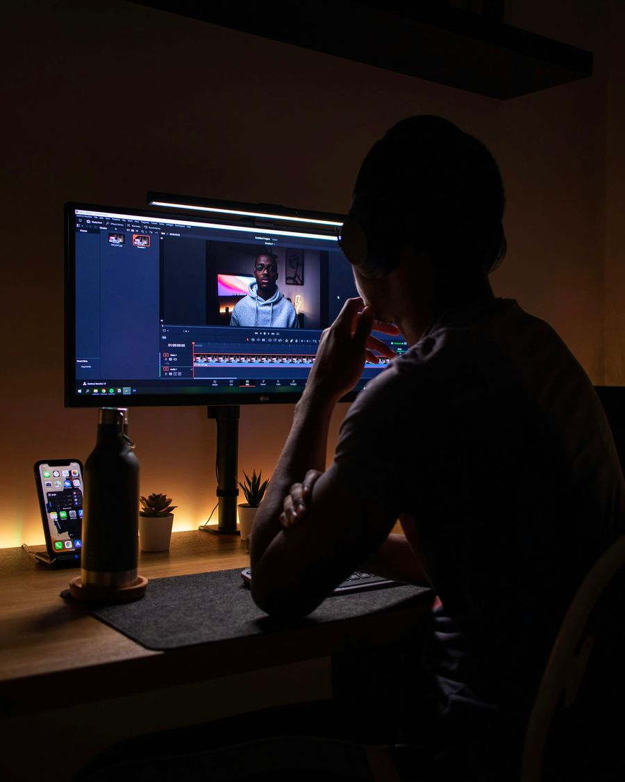 A creator wearing headphones editing video at a desk in a dark studio