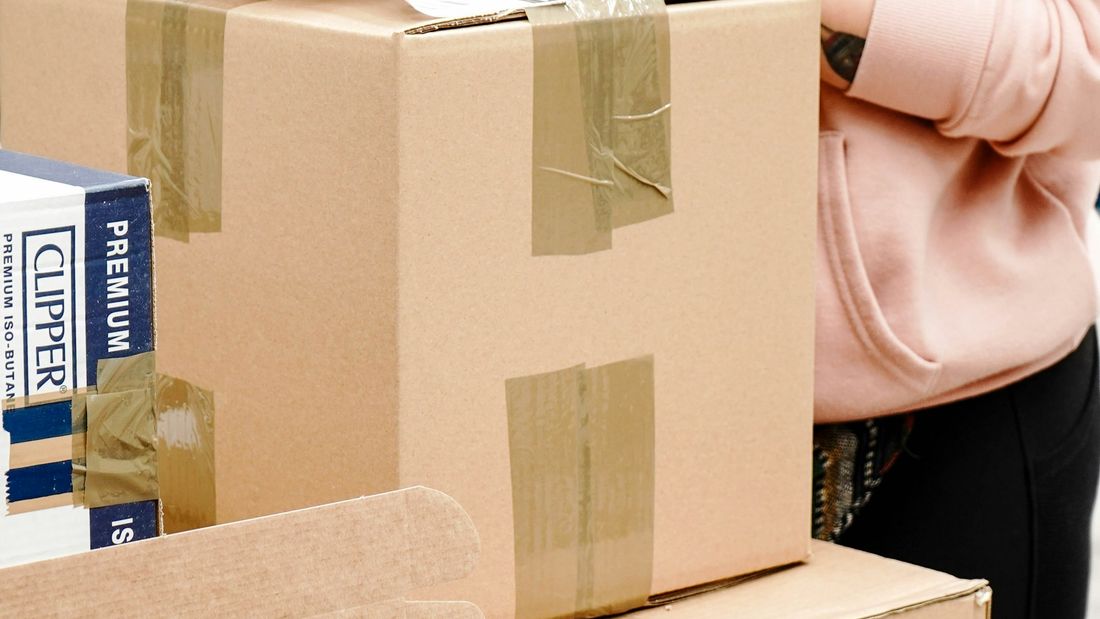 A young woman in a pink hoodie taping and labelling an online order at a packing bench