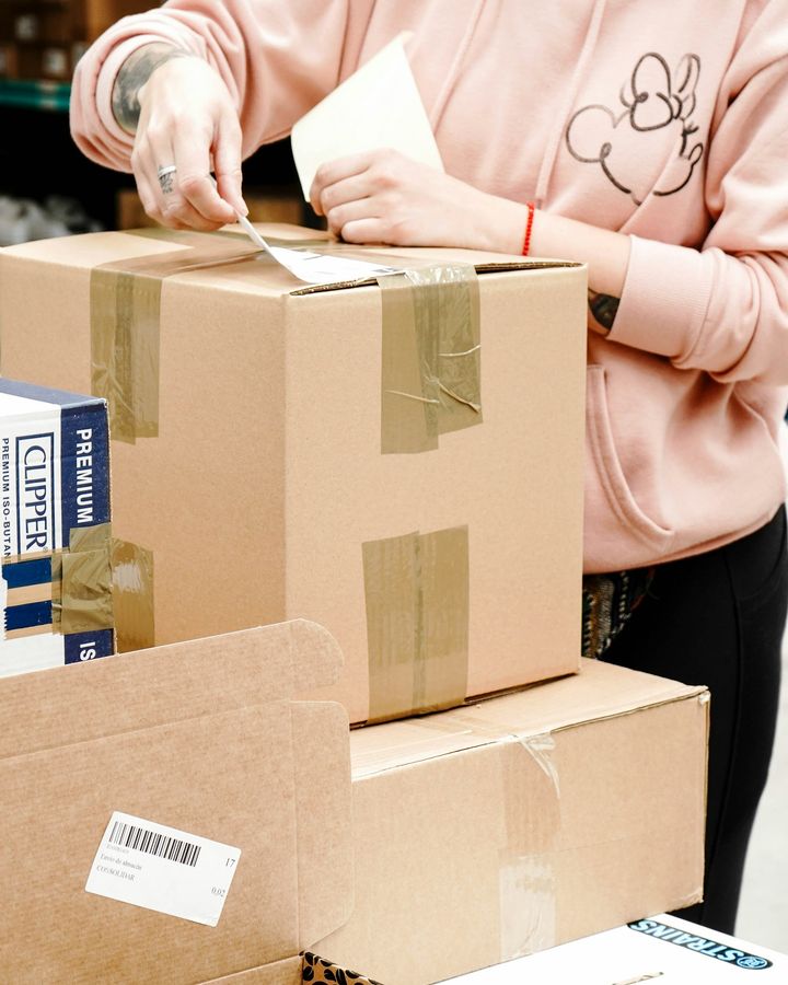 A young woman in a pink hoodie taping and labelling an online order at a packing bench